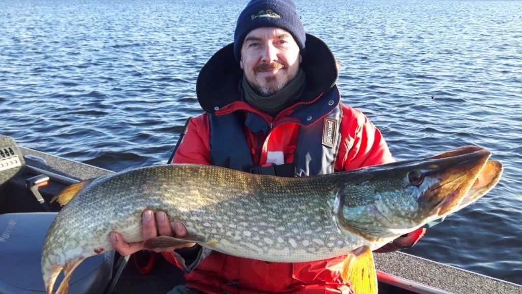 Chris Barry on a fishing boat holding a pike